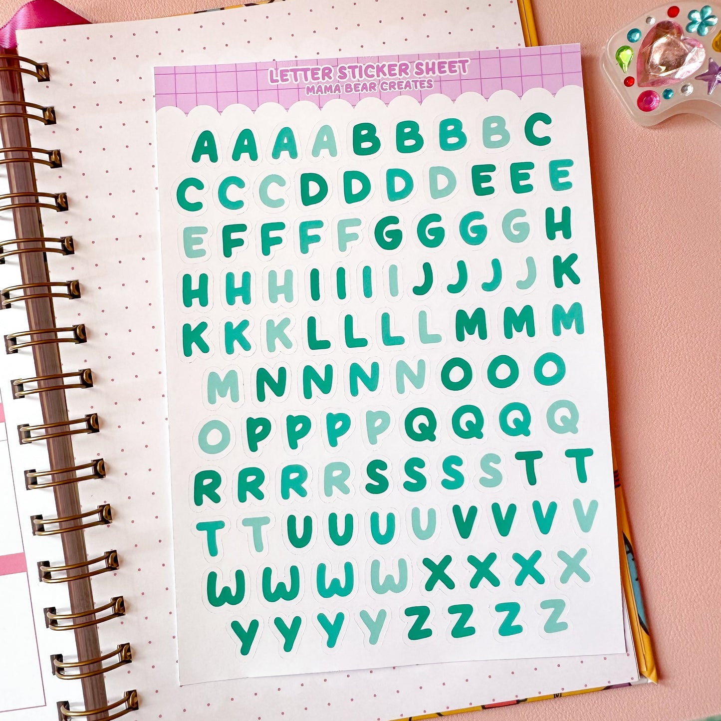 Sheet of letter stickers with a colorful border on a pink surface with stationery items.