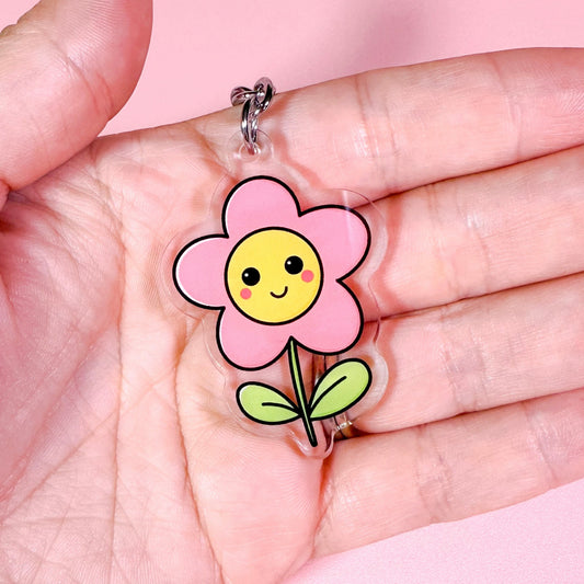 Flower-shaped keychain with a smiley face held in a hand against a pink background