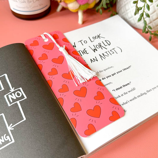 Open book with a pink bookmark featuring red heart patterns on a pink surface.