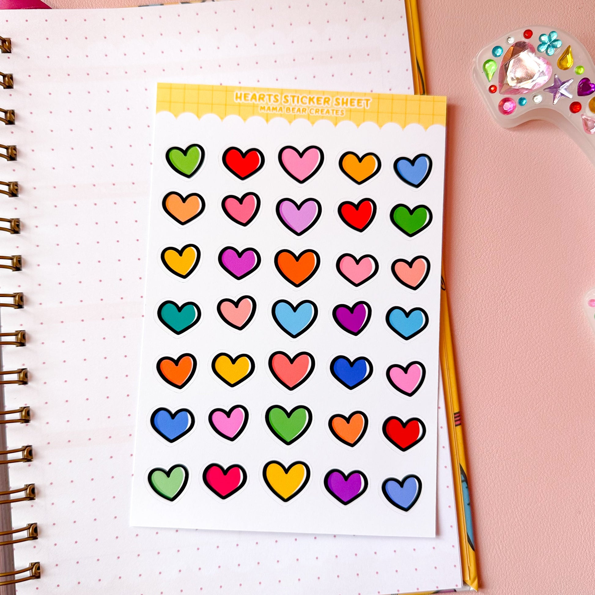 Sheet of colorful heart-shaped stickers on a notebook with stationery items.