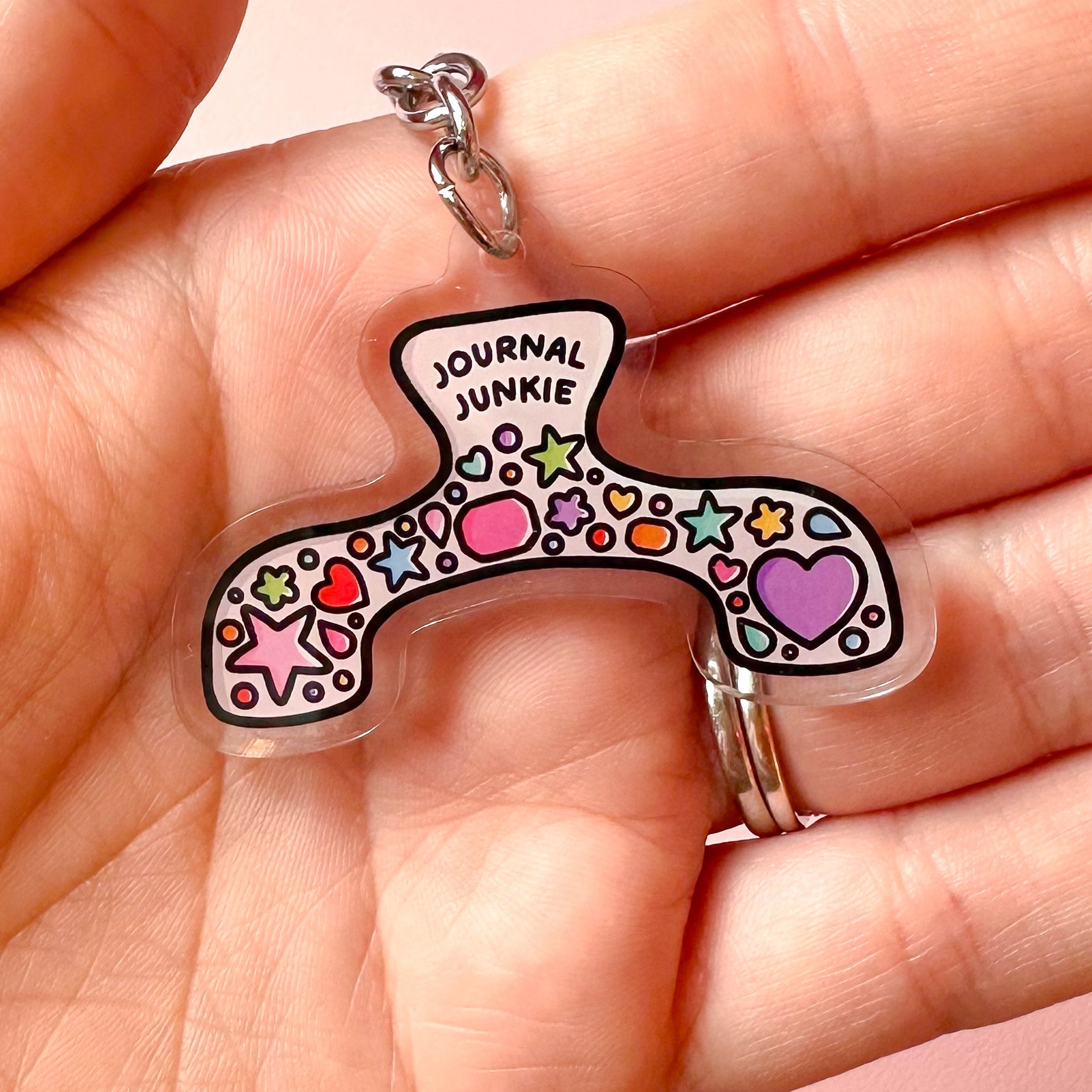 Colorful keychain with 'Journal Junkie' text held in a hand against a pink background