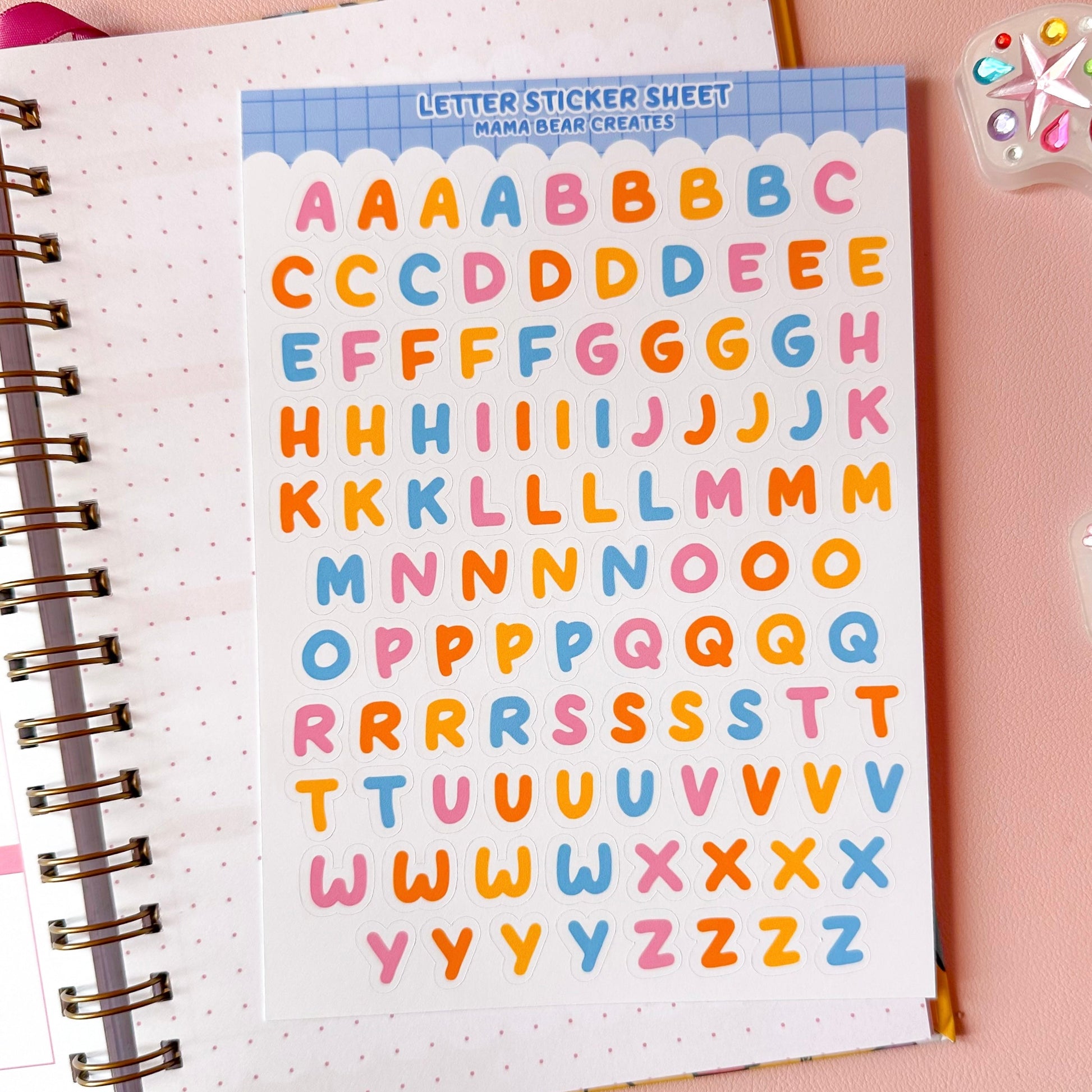 Sheet of colorful letter stickers on a notebook with stationery items around.