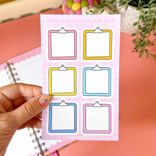 Sheet of large clipboard stickers held by a hand with a notebook and decorative items in the background.