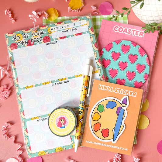 Stationery items including a notepad, coasters, and a vinyl sticker on a pink surface with decorative elements.