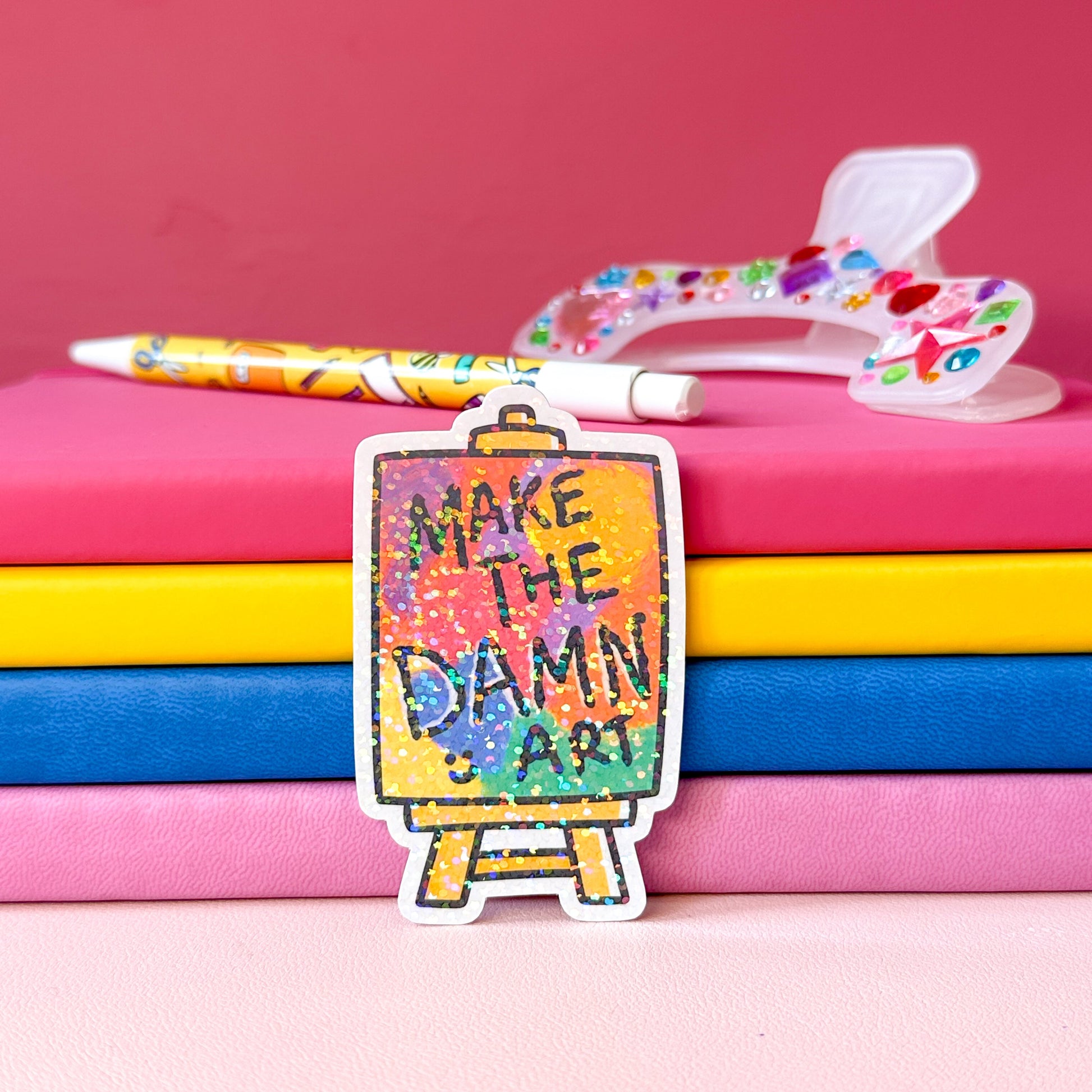 Colorful canvas sticker saying 'Make the Damn Art' on a pink background