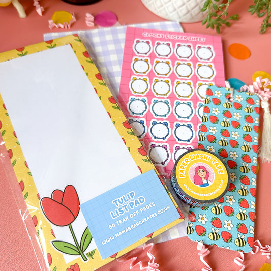 Colorful stationery items including a notepad, stickers, and a small container on a pink surface.
