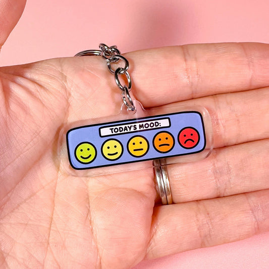 Keychain with emoji faces held in a hand against a pink background