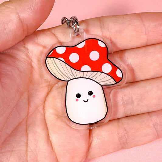 Mushroom-shaped keychain with a red polka dot cap held in a hand against a pink background