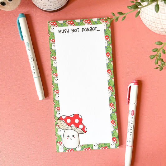 Notepad with mushroom design and two pens on a pink surface