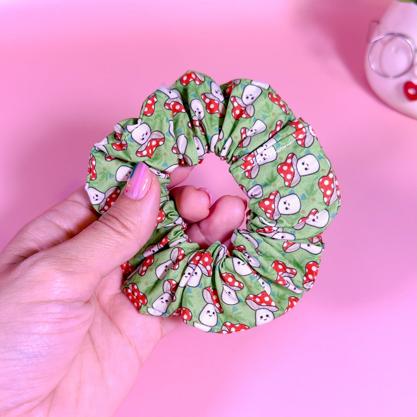 Hand holding a green scrunchie with cartoon character pattern on a pink background