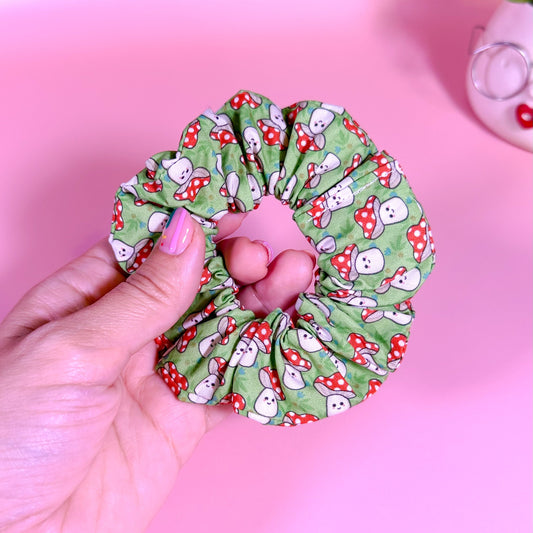 Hand holding a green scrunchie with cartoon character pattern on a pink background