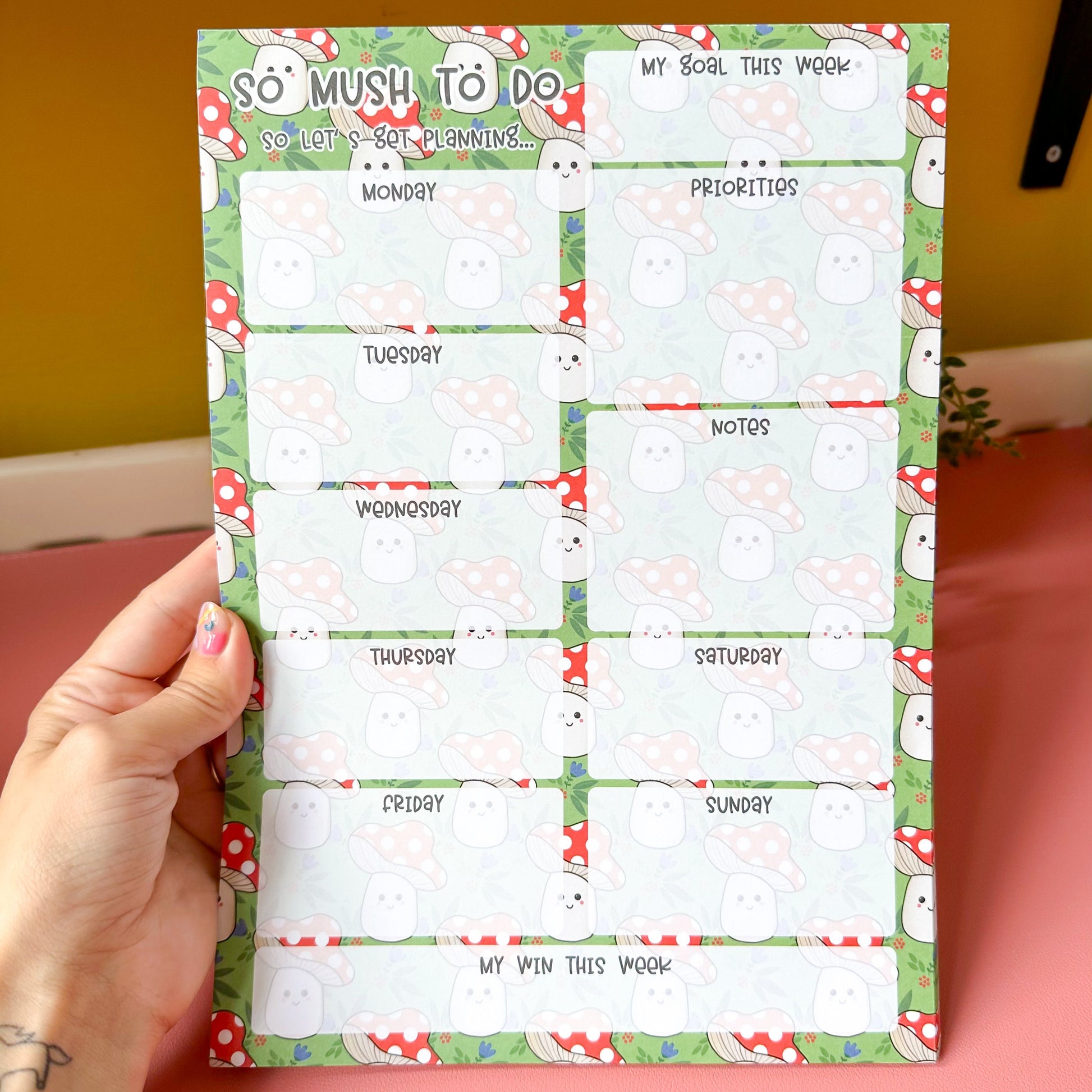 Weekly planner sheet with cartoon mushroom design held by a person.