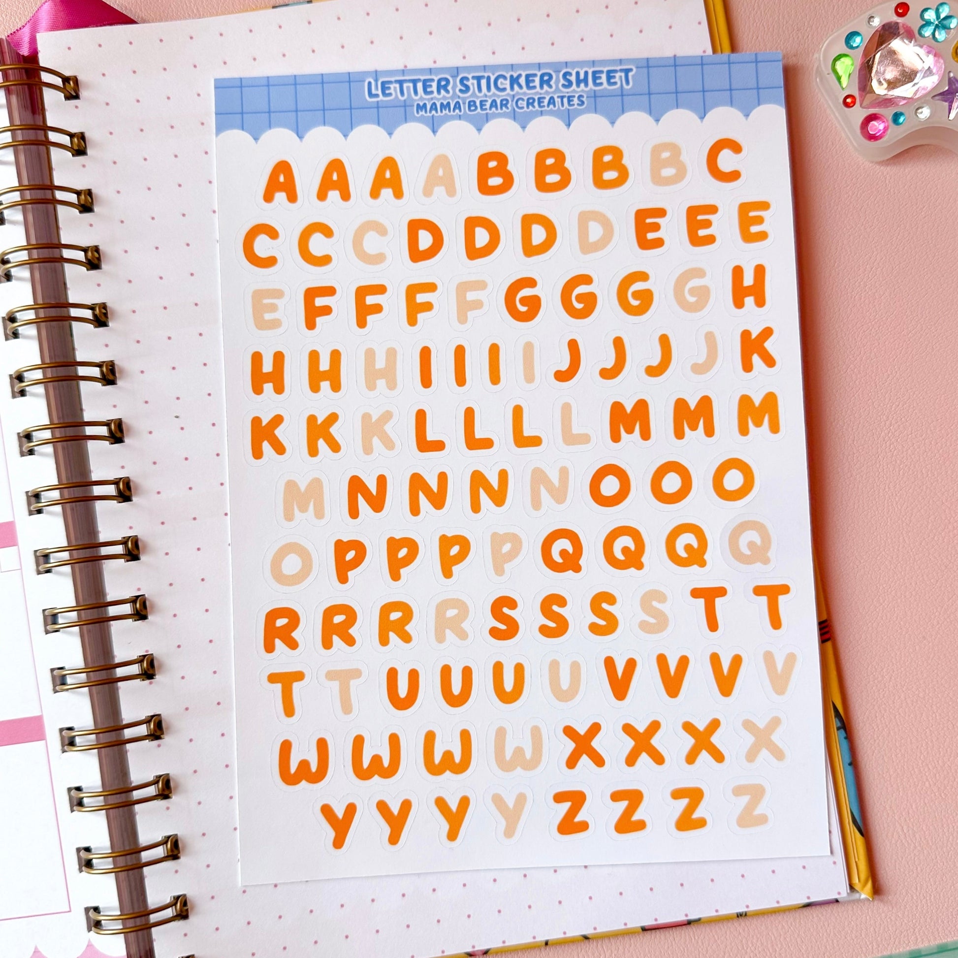 Sheet of letter stickers with a colorful border on a pink surface with stationery items.