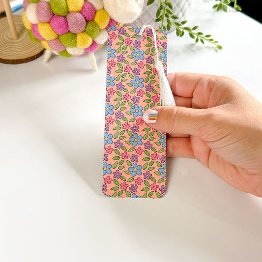 A hand holding a floral-patterned bookmark with a velvet-touch finish and rounded corners.