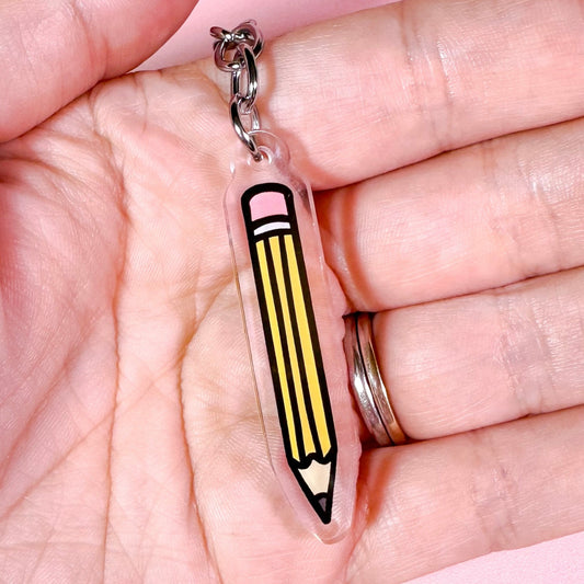Pencil-shaped keychain held in a hand against a pink background