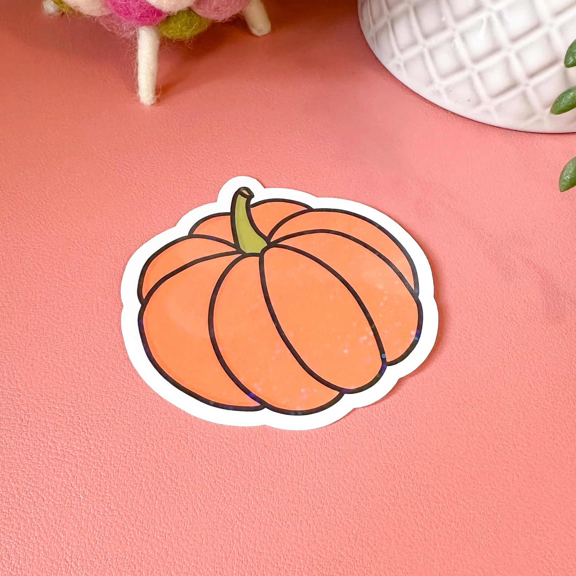 Pumpkin-shaped sticker on a pink surface with decorative items in the background