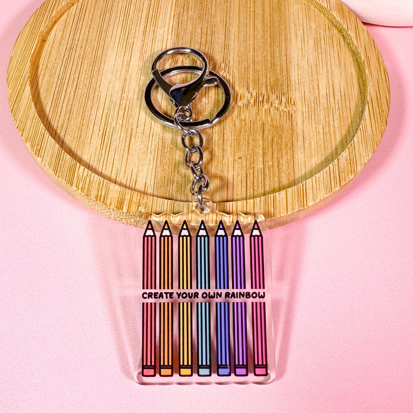 Keychain with colorful pencil-shaped charms on a wooden board with a pink background