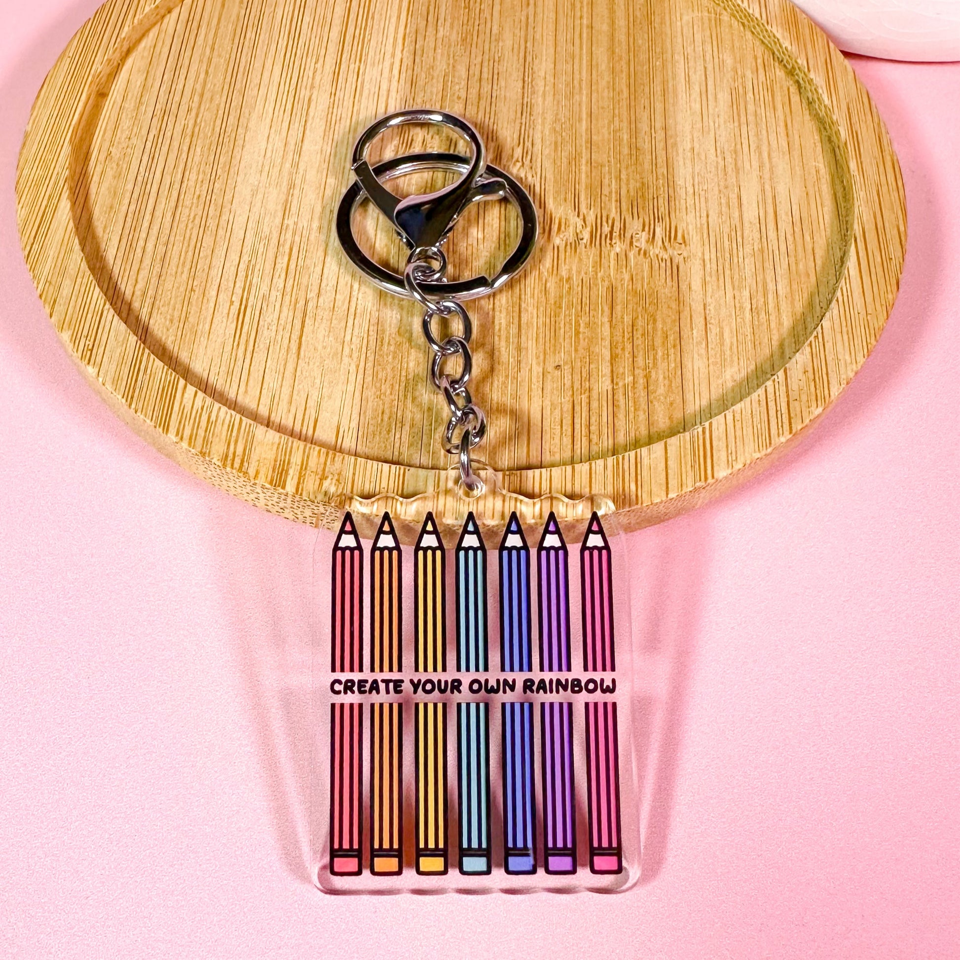 Keychain with colorful pencil-shaped charms on a wooden board with a pink background