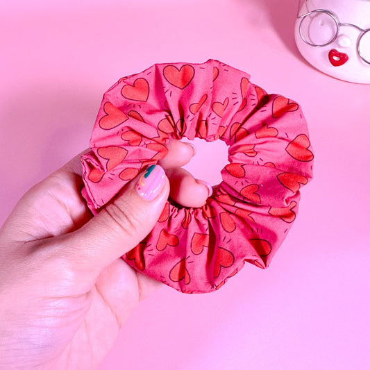 Hand holding a pink scrunchie with heart pattern on a pink background