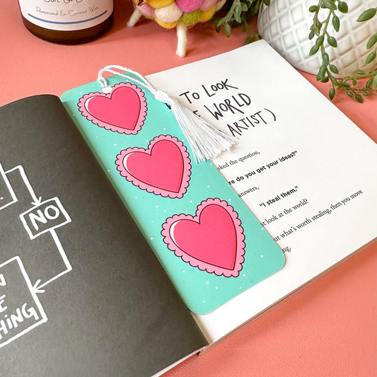 Open book with heart bookmark on a pink surface, next to a bottle of Belles salt and pepper.