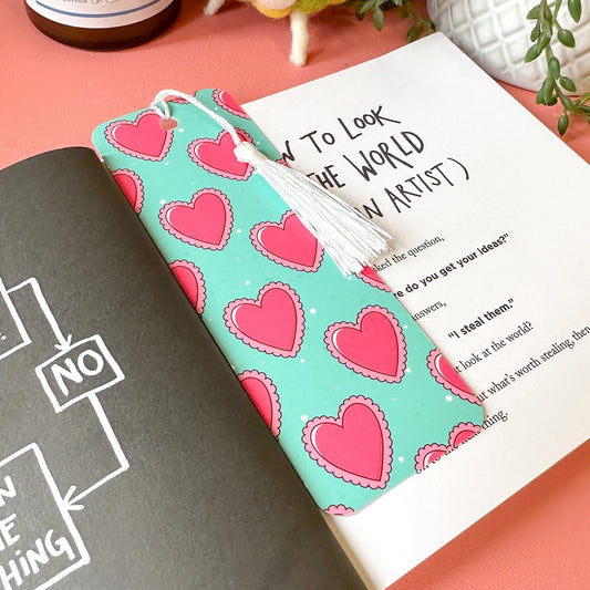 bookmark with heart pattern on a pink surface with a plant and bottle in the background