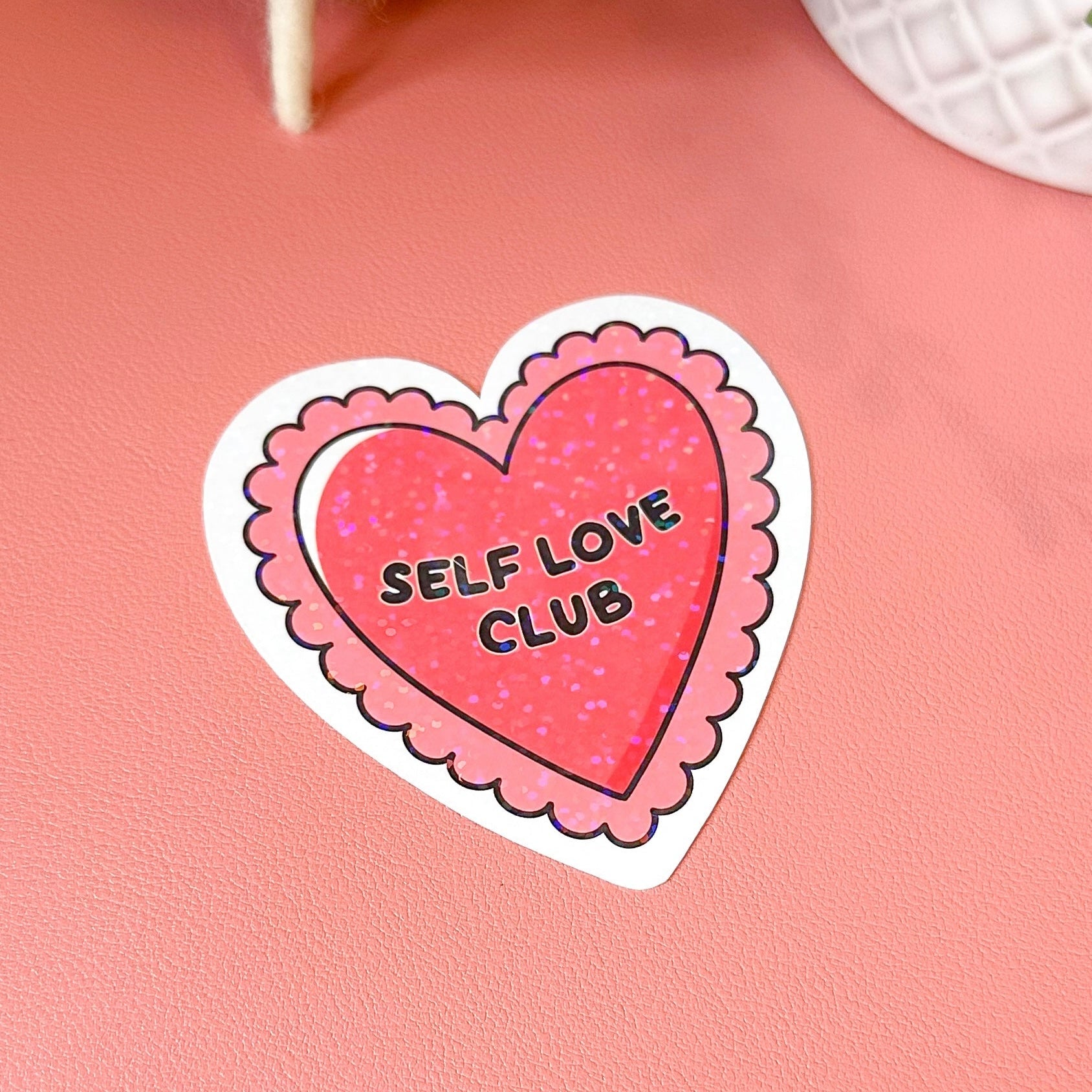 Heart-shaped sticker with 'Self Love Club' text on a pink background