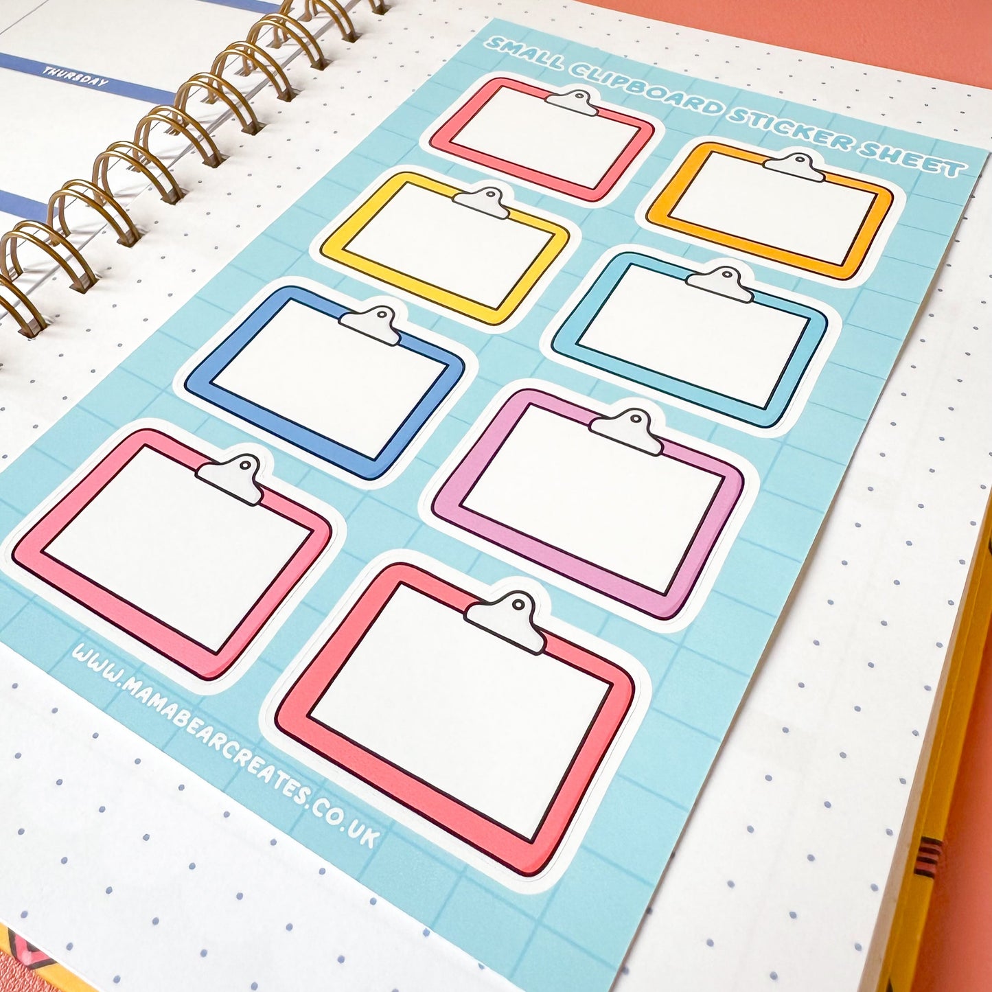 Colorful clipboard stickers on a planner page with a pen on a pink surface.