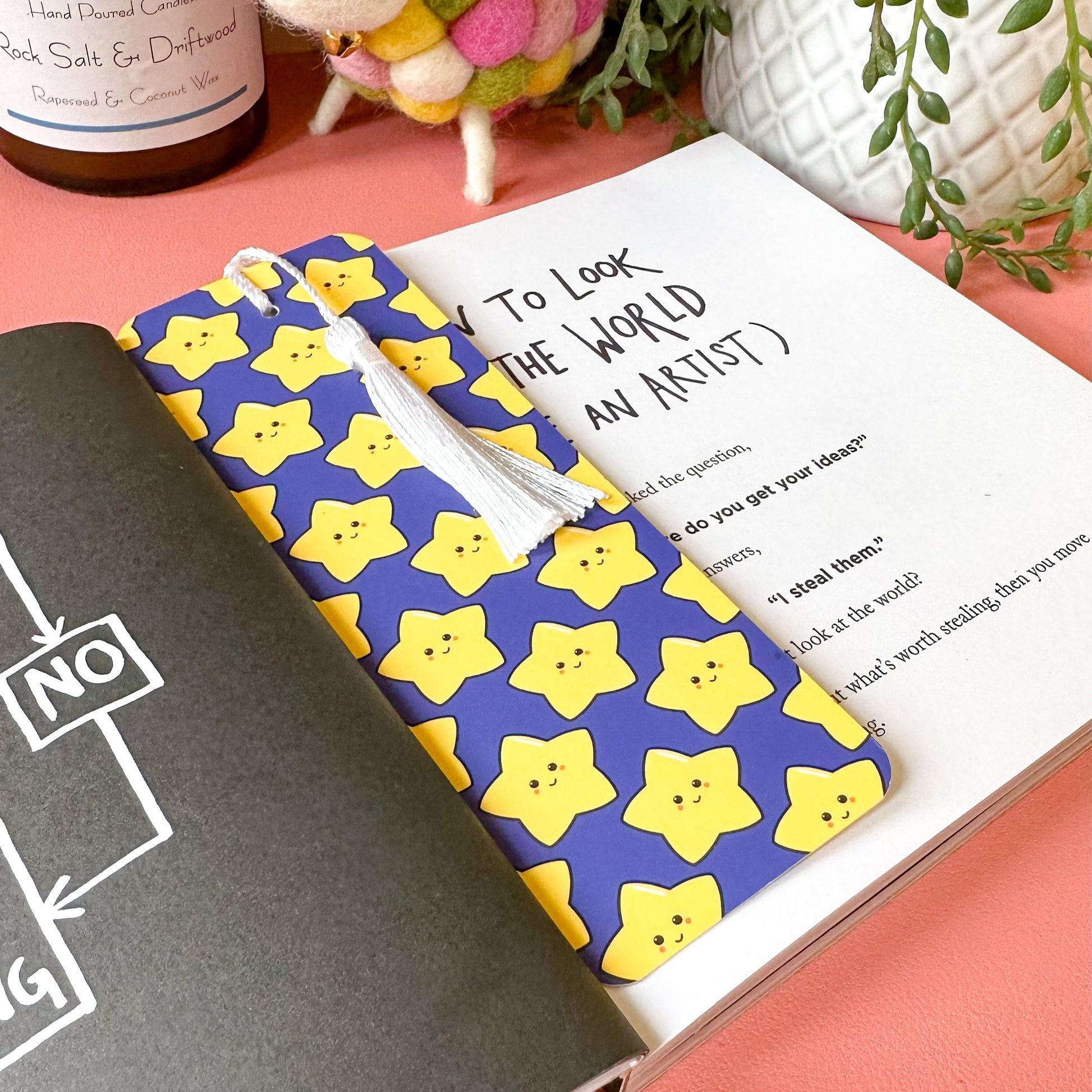 bookmark with a colorful star pattern cover on a pink surface with a plant and bottle in the background.