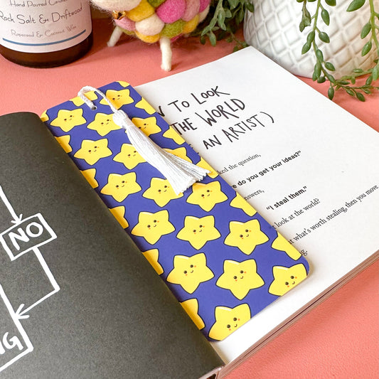 bookmark with a colorful star pattern cover on a pink surface with a plant and bottle in the background.