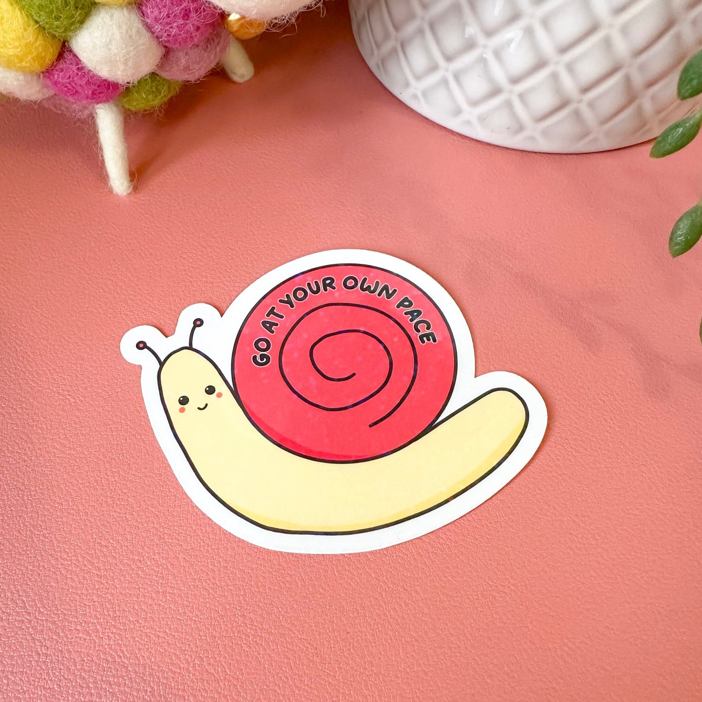 Sticker of a snail with a pink spiral shell on a pink surface.