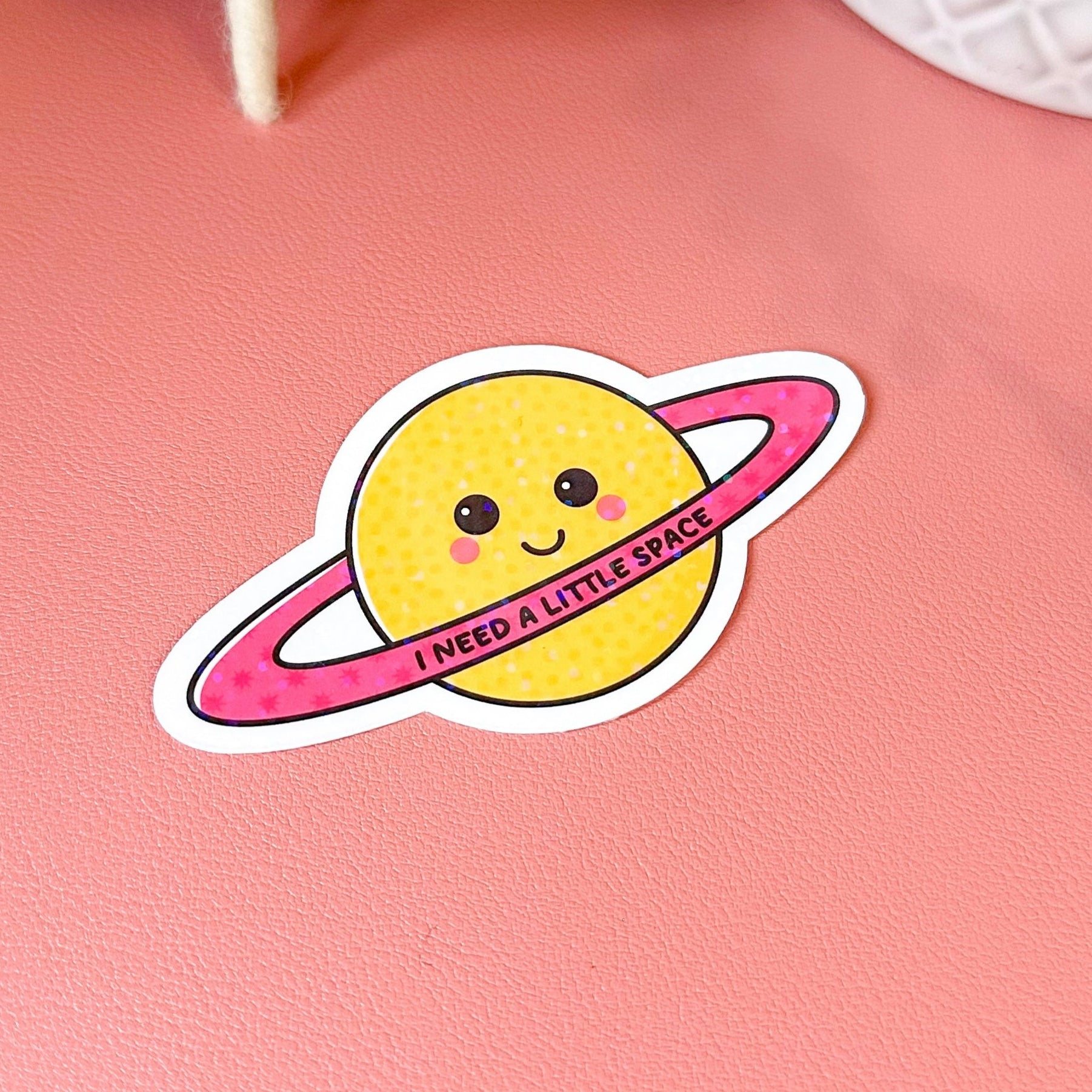 Sticker of a smiling planet with a pink ring on a pink background