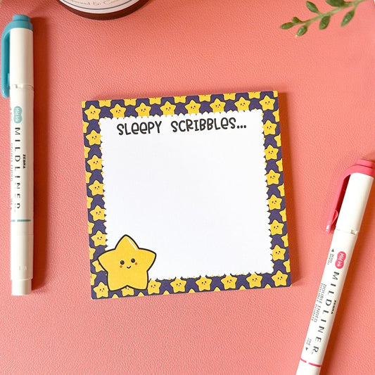 Notepad with star design and 'Sleepy Scribbles' text on a pink background with pens.