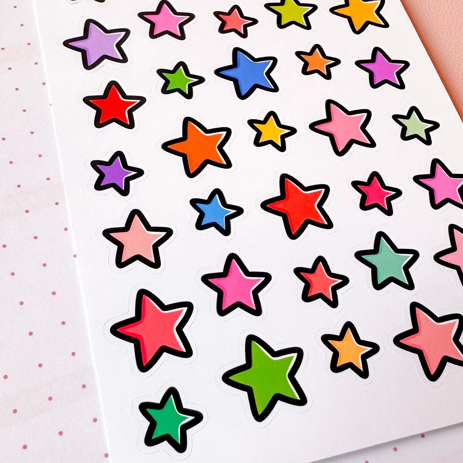 Colorful star-shaped stickers on a white sheet with pink dots.