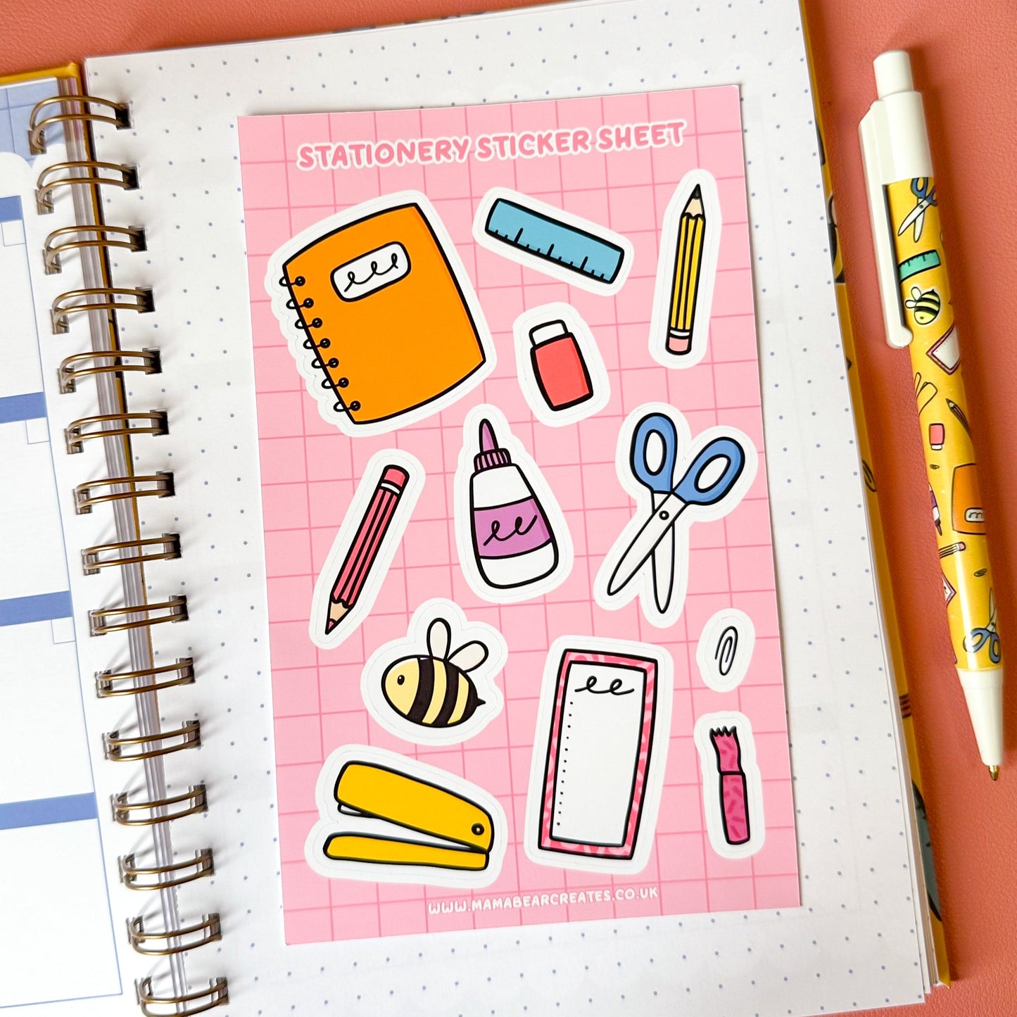 Stationery stickers sheet on a notebook with a pen on a pink background