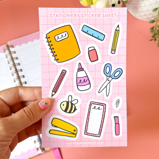 Sheet of stationery-themed stickers held by a hand on a pink background