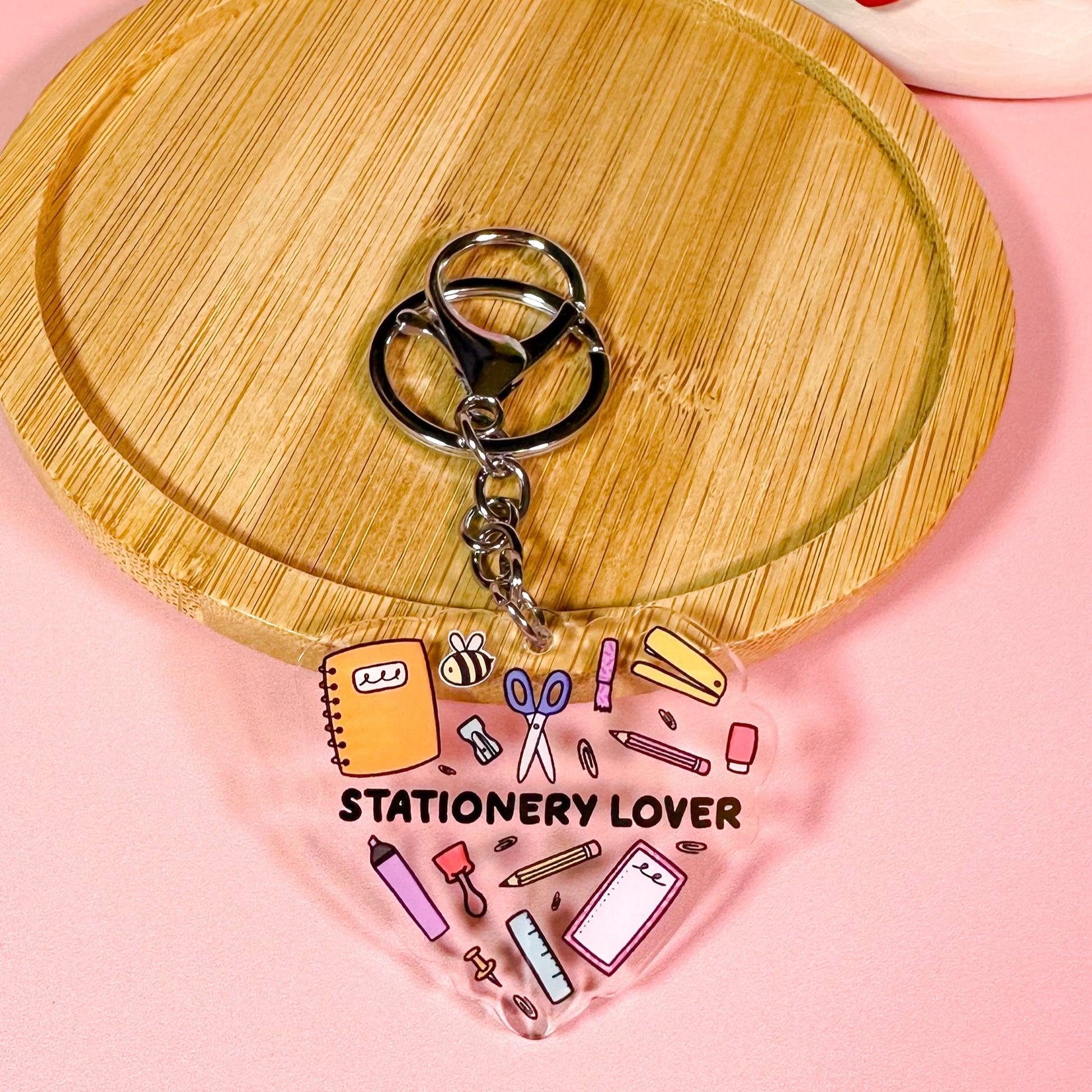 Keychain with stationery-themed design on a wooden stand against a pink background