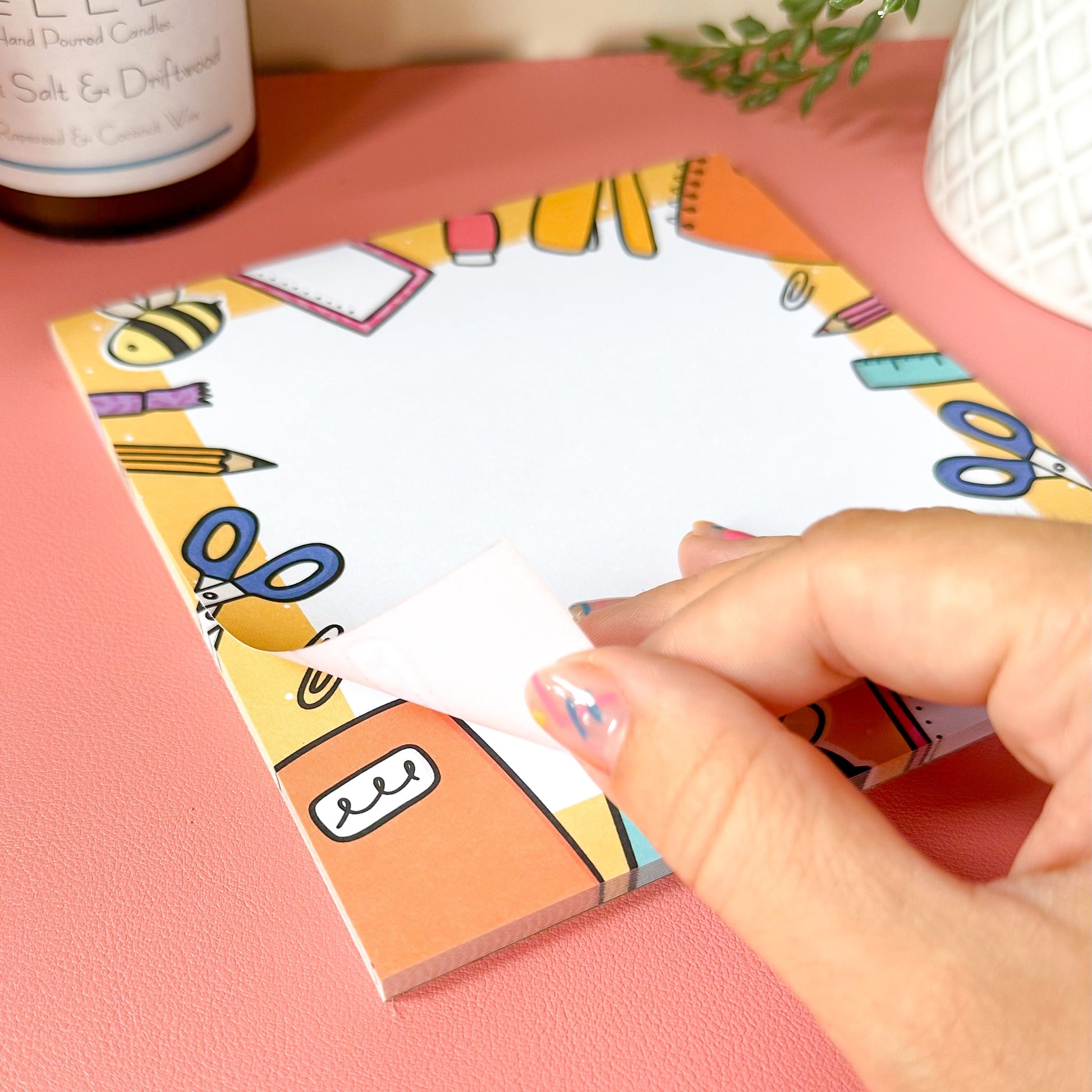 Hand holding a colorful notepad with cartoon designs on a pink surface.