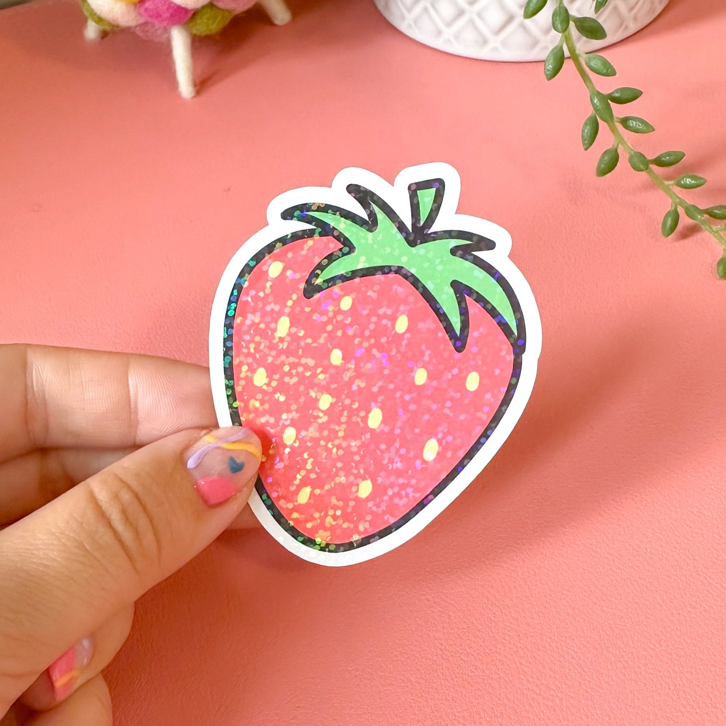 Hand holding a strawberry-shaped sticker with a pink background