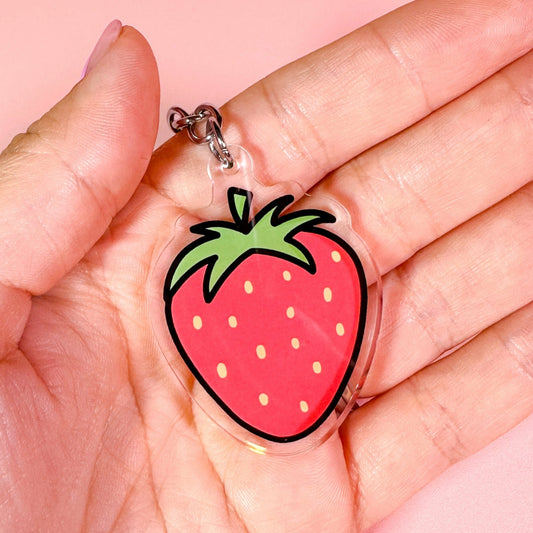 Strawberry-shaped keychain held in a hand against a pink background