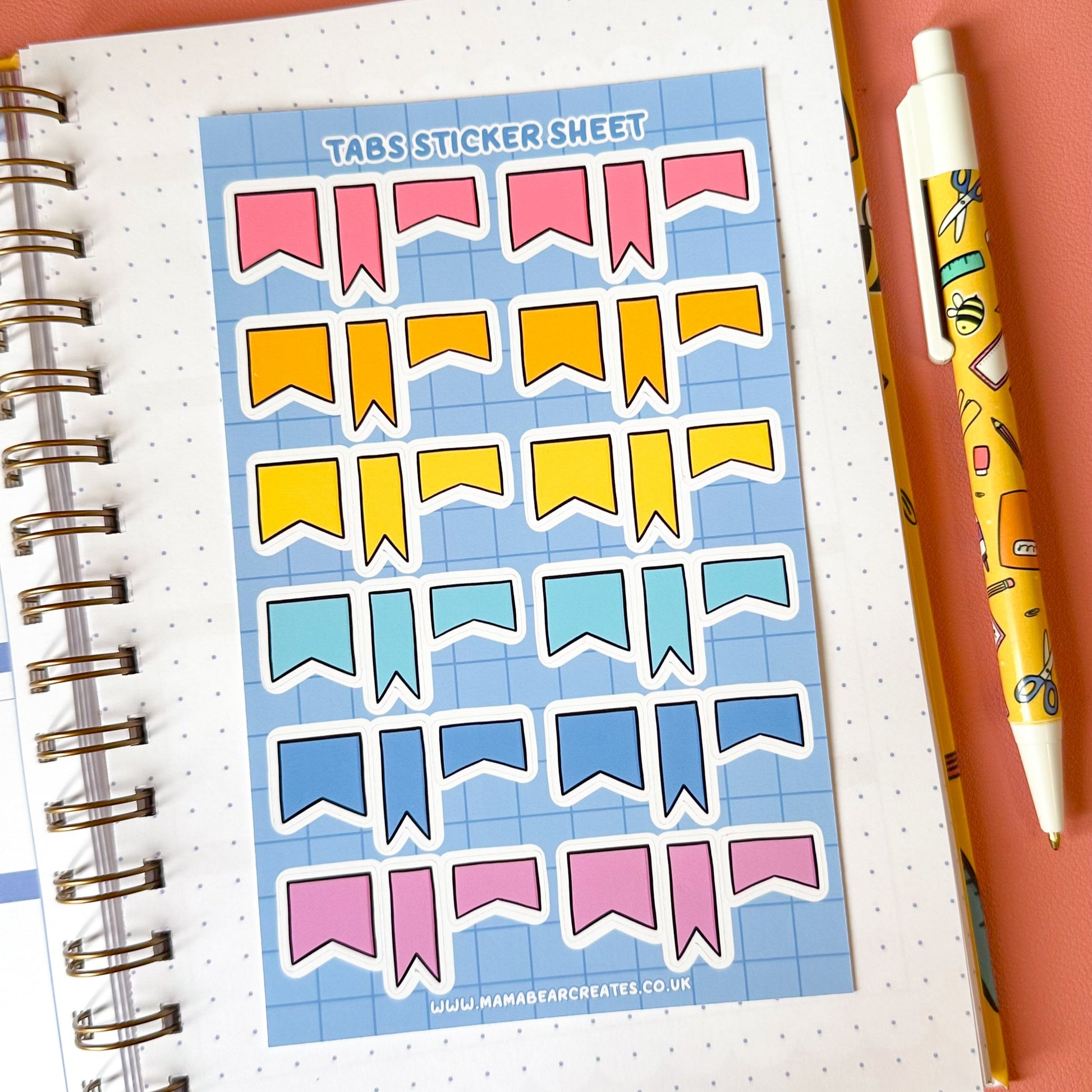 Sheet of colorful banner stickers on a notebook with a pen on a pink background
