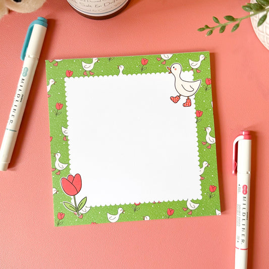 Notepad with a floral design on a pink surface with pens and a candle.