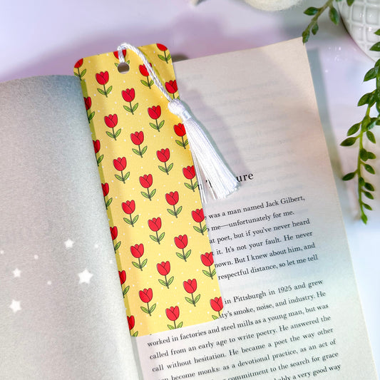 A yellow bookmark with a pattern of red tulips and green leaves, featuring a white tassel, is placed on an open book.