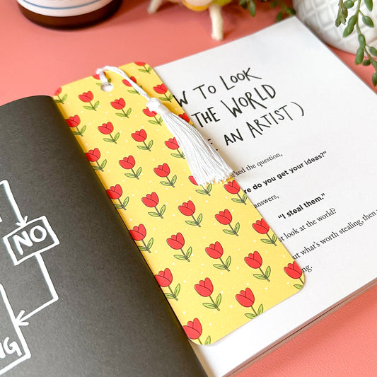 tulip bookmark on a pink surface with a candle and plant in the background.