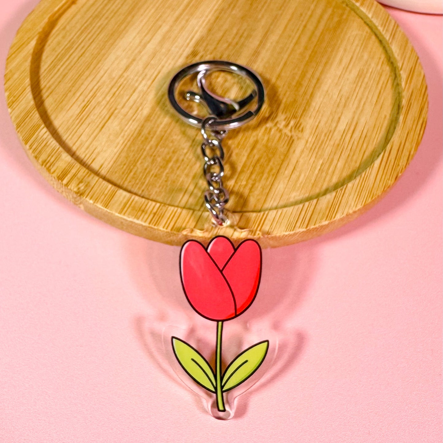 Keychain with a red tulip design on a wooden board with a pink background