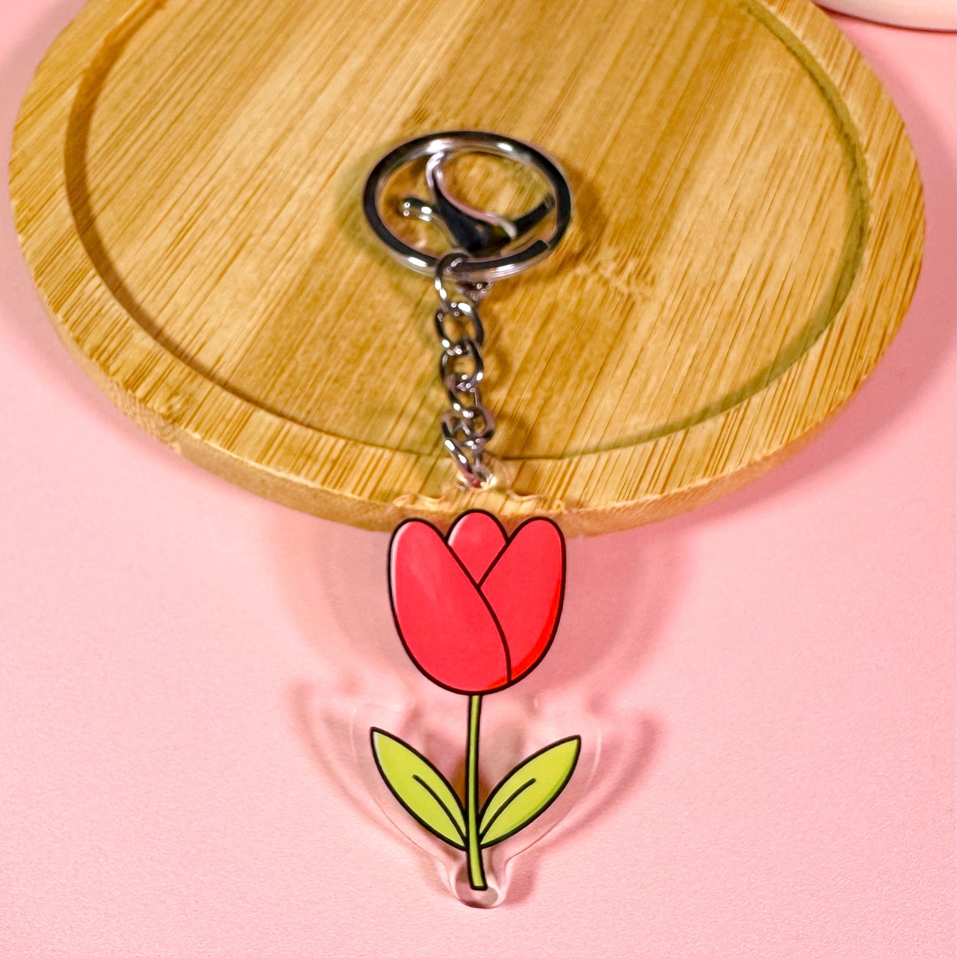 Keychain with a red tulip design on a wooden board with a pink background