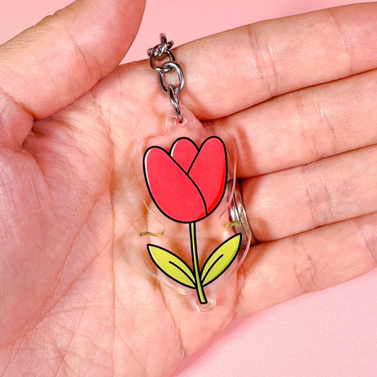 Keychain with a red tulip design held in a hand against a pink background