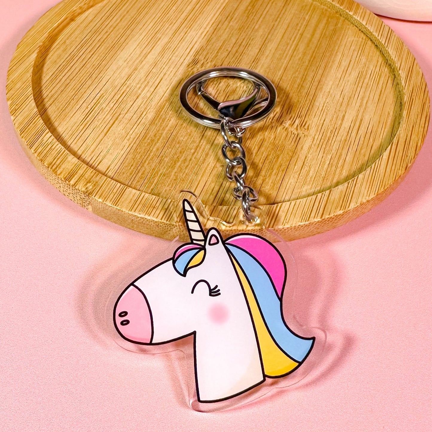 Unicorn-shaped keychain on a wooden coaster with a pink background