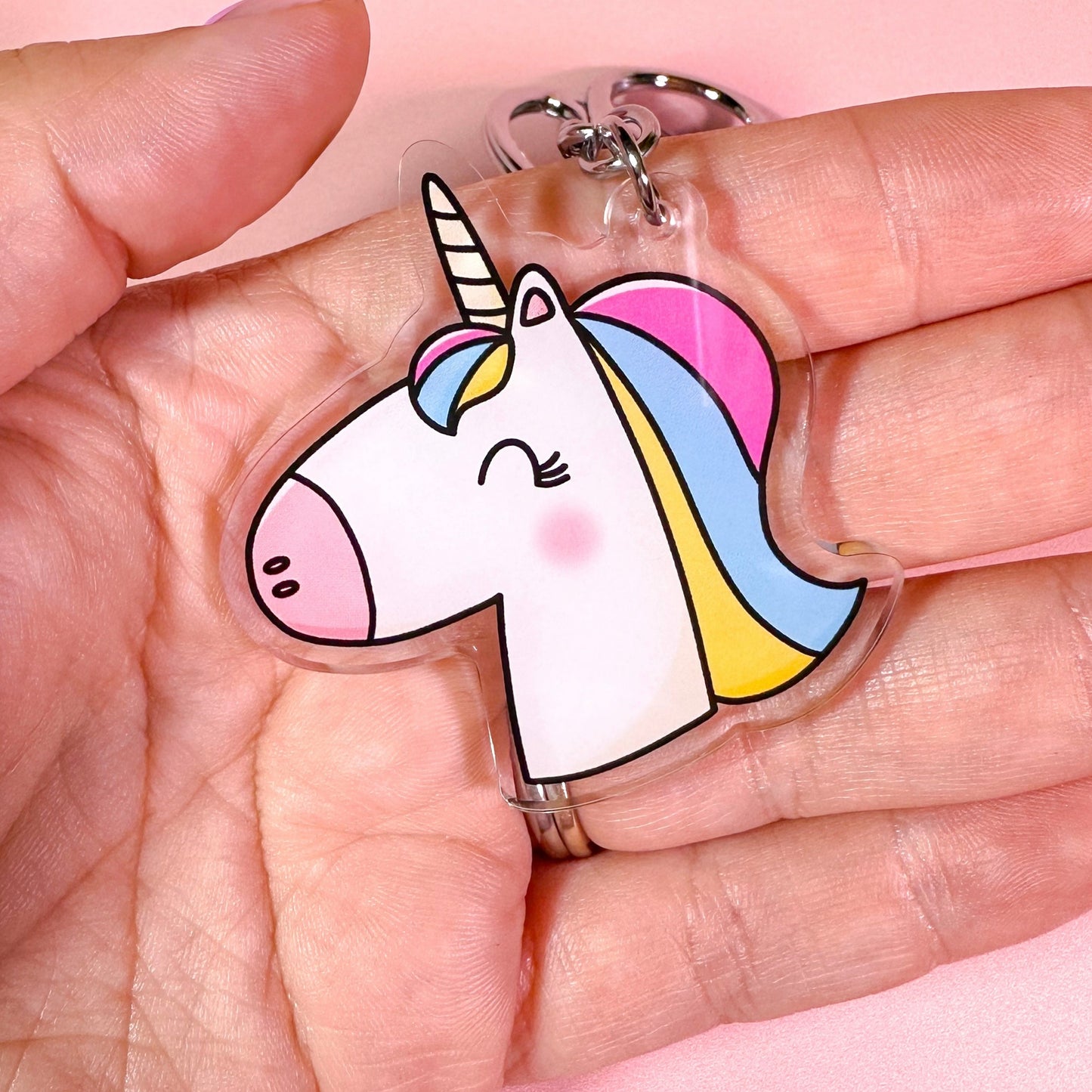 Unicorn-shaped keychain held in a hand against a pink background