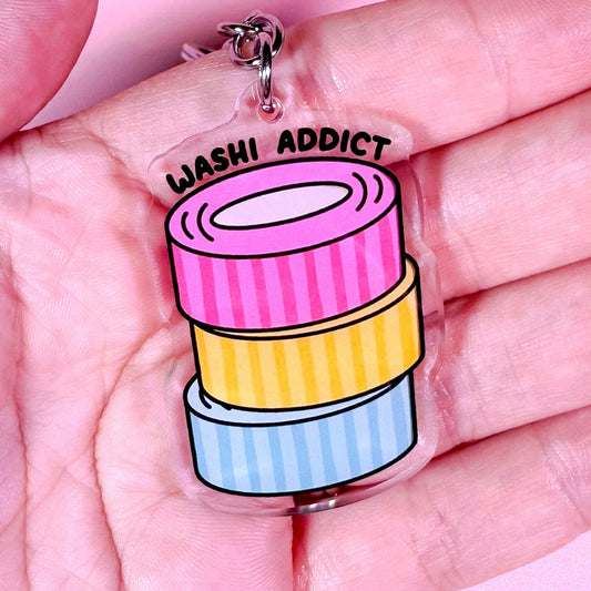 Keychain with cartoon-style washi tape design and 'Washi Addict' text held in a hand against a pink background.
